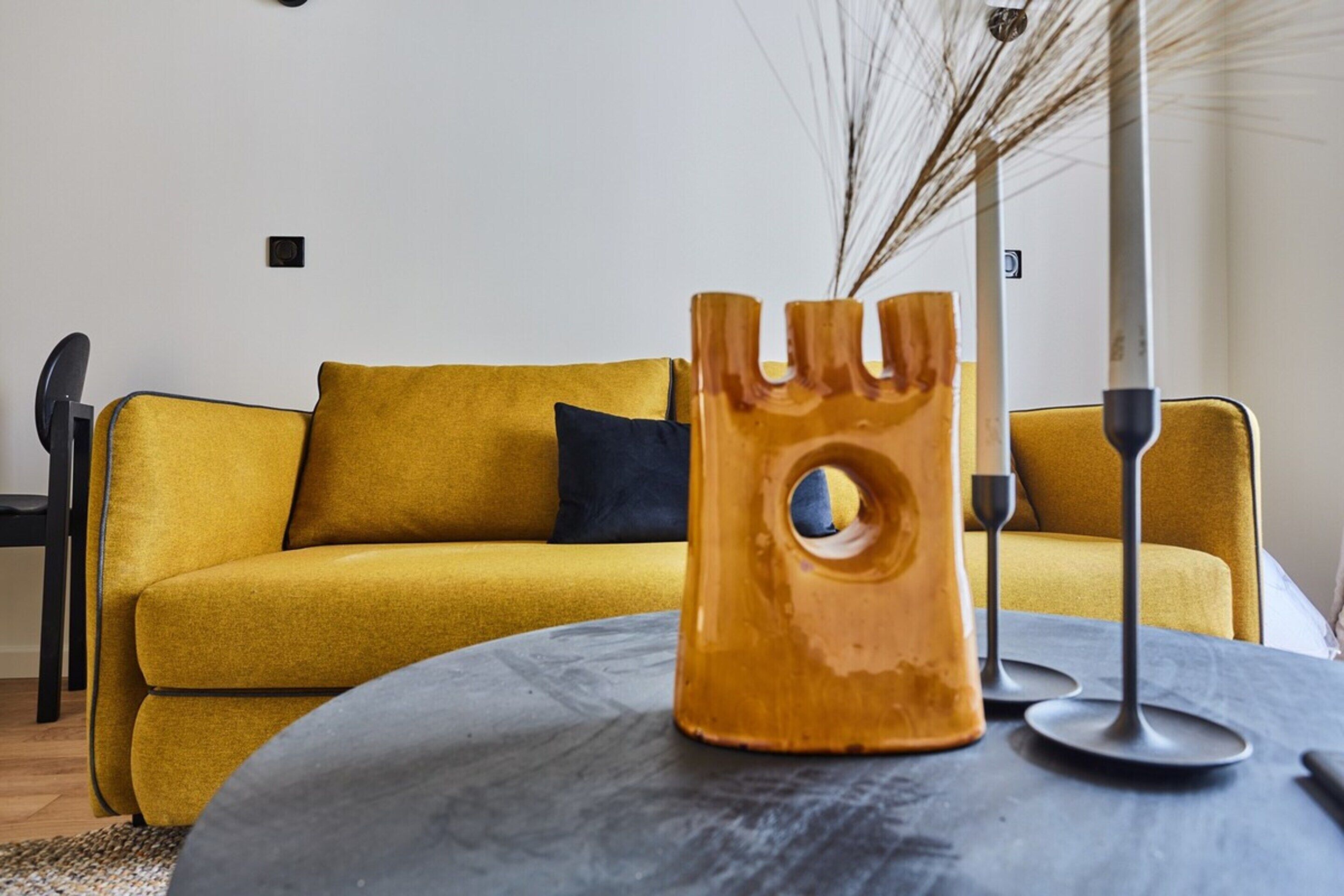 Ein modernes Wohnzimmer mit einem gelben Sofa, einem runden Tisch und einer dekorativen Vase.