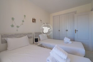 Une chambre d’hôtel avec deux lits, du linge de lit blanc, une table de chevet avec une lampe et un élément décoratif mural.