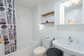 Une salle de bain avec des toilettes blanches, un lavabo, un miroir et un rideau de douche à motifs.