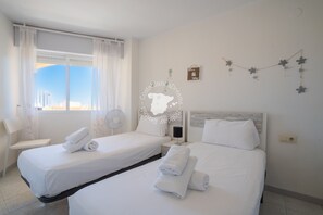 Une chambre d’hôtel avec deux lits, une chaise, un bureau et une fenêtre avec des rideaux.