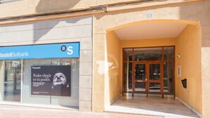 De ingang van een gebouw met een blauw bord met daarop Sabadell Solbank en een glazen deur.