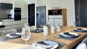 A modern dining area with a long wooden table set for six, surrounded by chairs. There are multiple wine glasses and plates on the table, and a kitchen area is visible in the background. - Villa Porto-Vecchio with swimming pool 8 persons (Lecci)