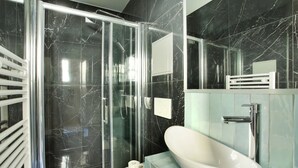 Un bagno moderno con cabina doccia in vetro, un lavandino bianco e una parete rivestita in marmo.