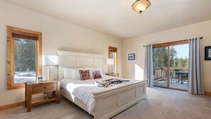 Ein Schlafzimmer mit einem großen Bett, Nachttischen aus Holz, einem Fenster mit Blick und einer Schiebetür zu einem Balkon.