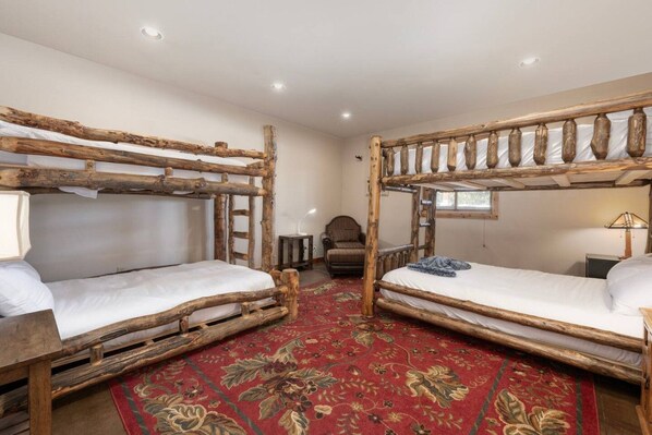 A room with two bunk beds made of wood, a red floral carpet, a small table, and a chair.