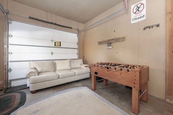A garage with a closed door, a foosball table, and a beige sofa.
