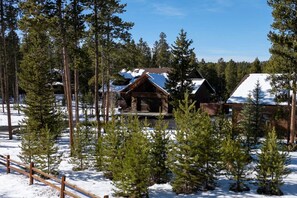 Eine Hütte, umgeben von verschneitem Gelände und Kiefern.