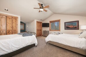 A bedroom with two beds, wooden wardrobes, a ceiling fan, a TV, and a window with a view of trees.