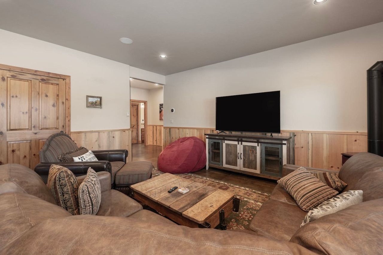 A living room with a large flat-screen TV, wooden cabinets, a red bean bag, and a brown leather sofa.