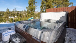 Ein Whirlpool mit einer Holzdar Terrasse und Blick auf eine verschneite Landschaft mit Bäumen.