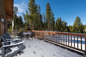 Um deck de madeira com mobiliário externo e vista para uma paisagem nevada.