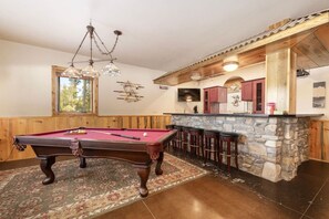 A pool table in a room with wooden walls and a stone bar area.