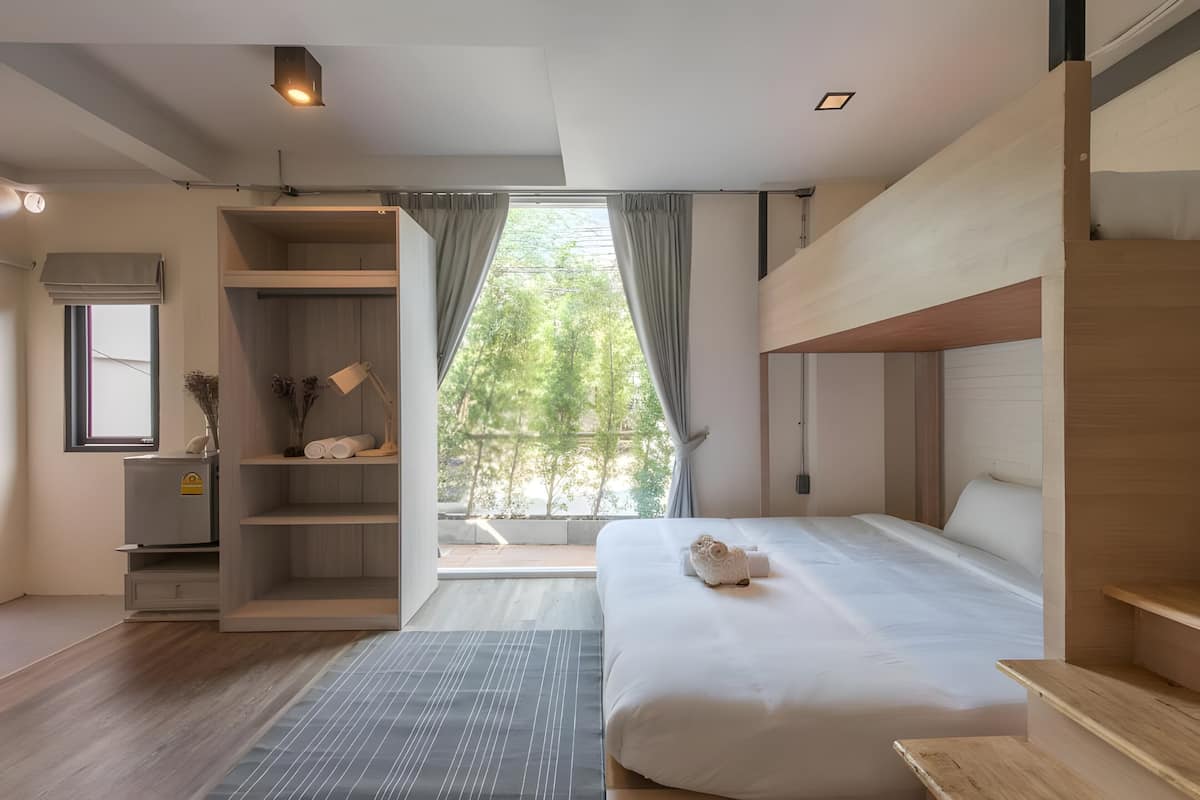 A modern hotel room with a large bed, a built-in wardrobe, a seating area with a view, and a window with curtains.