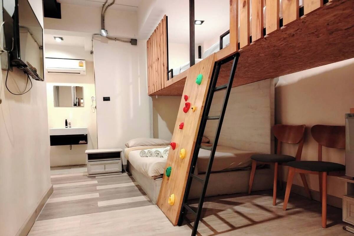 A modern bedroom with a bunk bed, a wooden climbing wall, a desk, and a chair.
