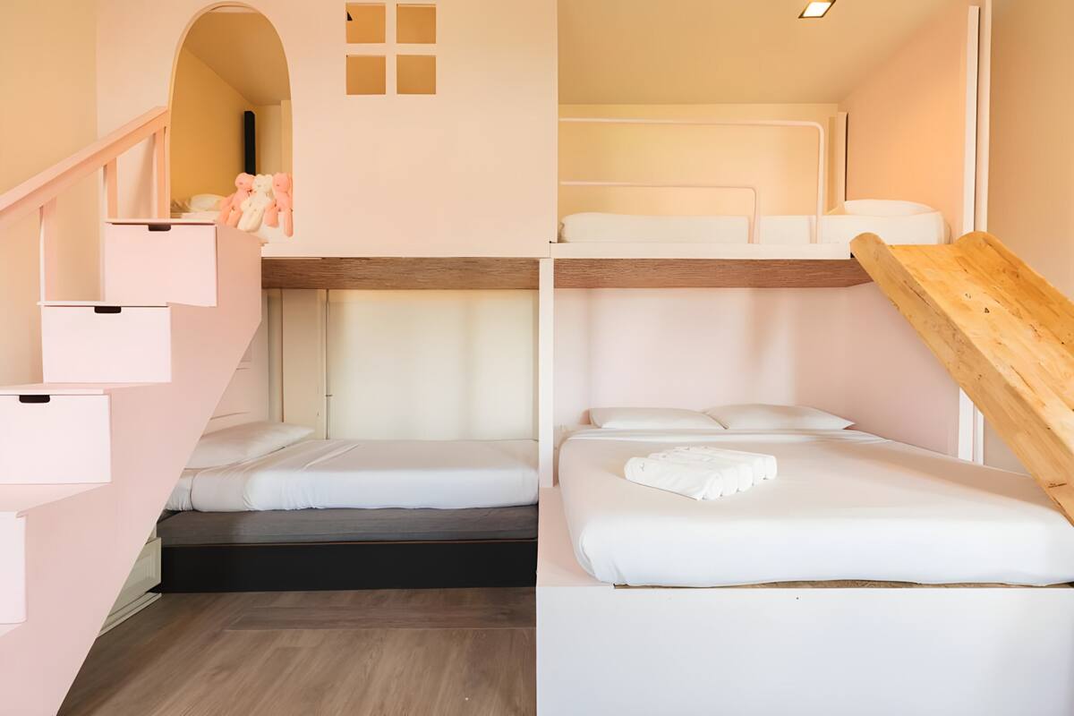 A compact room with bunk beds, a wooden staircase, and a small seating area with cushions.