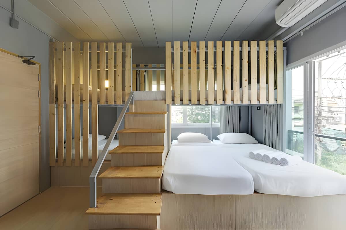 A modern hotel room with a wooden staircase, a bed with white linens, and a large window offering a view of the outdoors.
