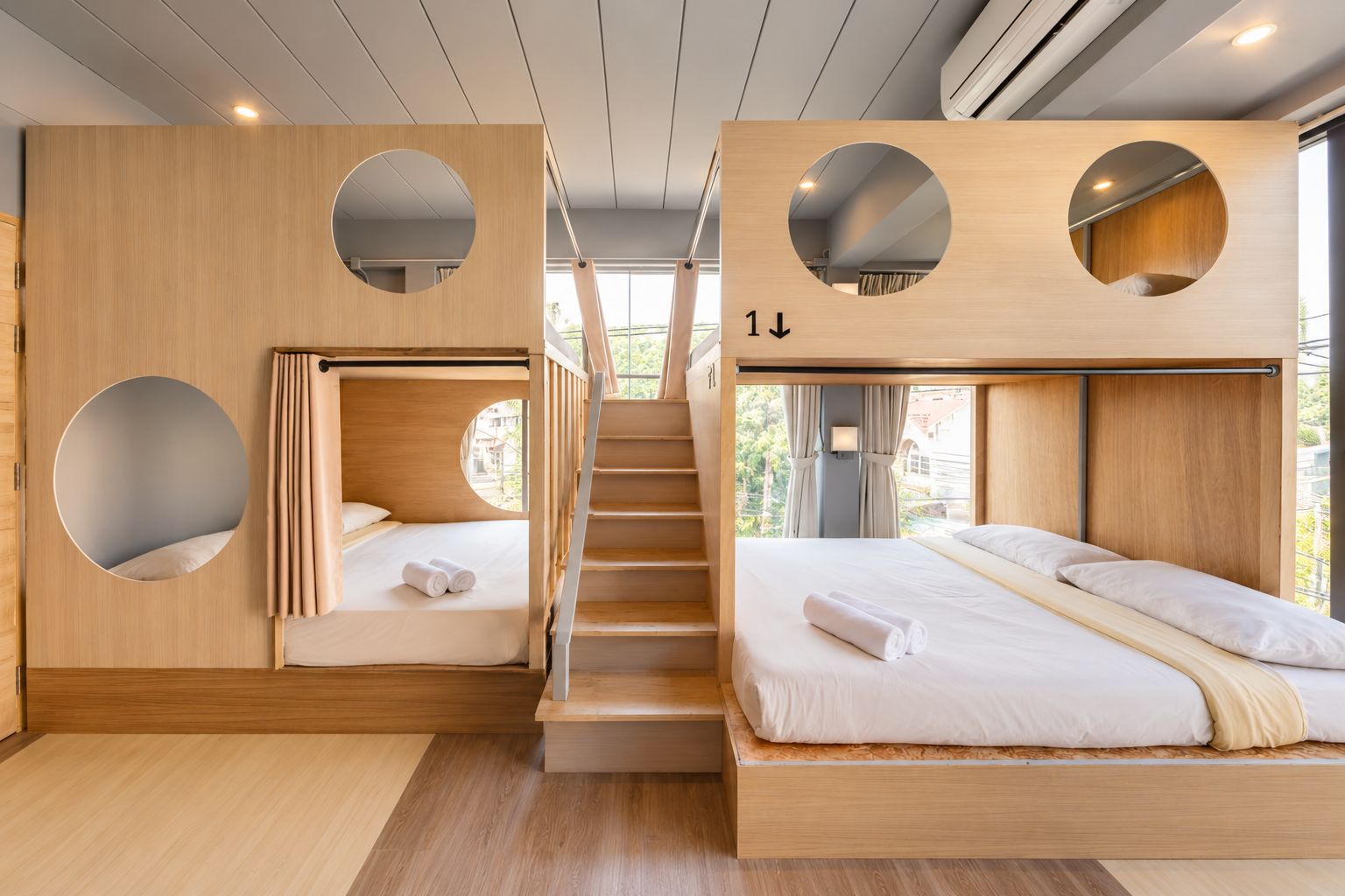 A modern hotel room with a bunk bed, a circular window, and a staircase.
