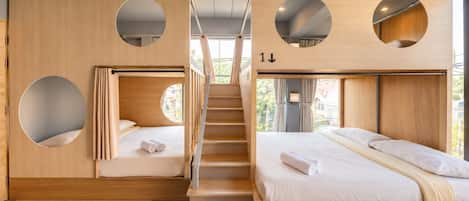 A modern hotel room with a bunk bed, a circular window, and a staircase.