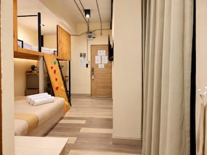 A hotel room with a bunk bed, a wooden ladder, a desk, and a door with a notice.