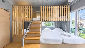 Quarto de hotel moderno com escada de madeira, cama com roupa de cama branca e uma grande janela com vista para a cidade.
