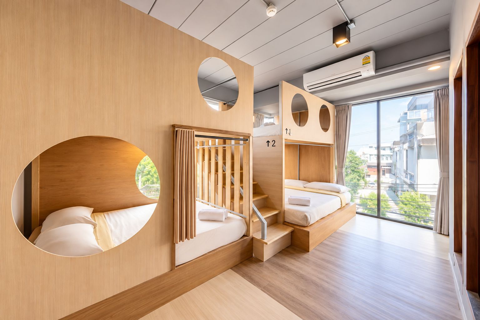 A modern hotel room with a wooden interior, a staircase, and a large window offering a city view.