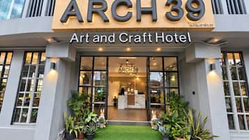 Exterior do ARCH 39 Art and Craft Hotel, com entrada visível, plantas em vasos e gramado sintético verde.