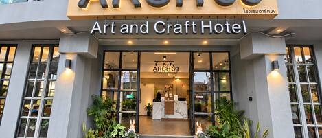 The exterior of ARCH 39 Art and Craft Hotel with a clear entrance, potted plants, and a green artificial lawn.