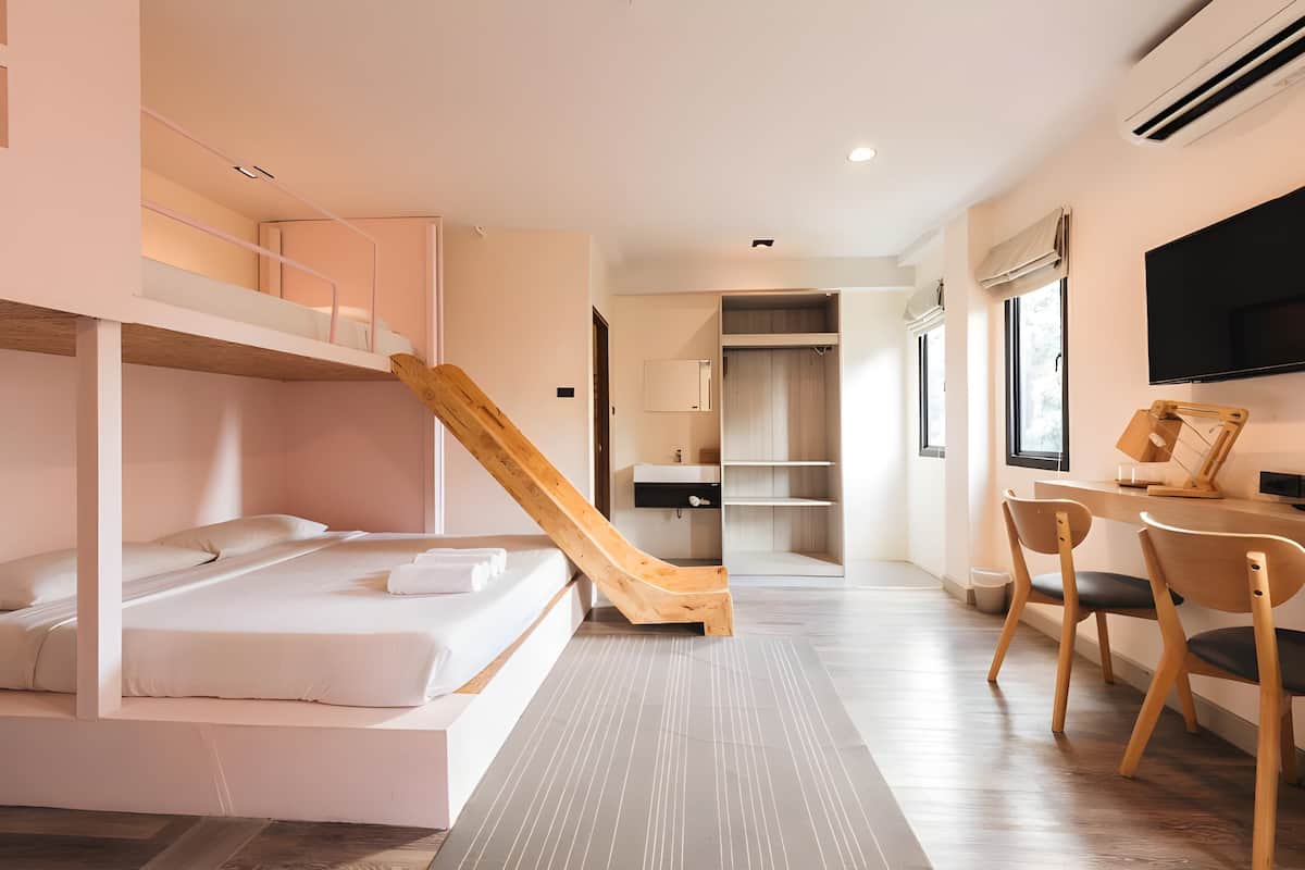 A modern hotel room with a bunk bed, a wooden slide, a desk with chairs, and a TV.