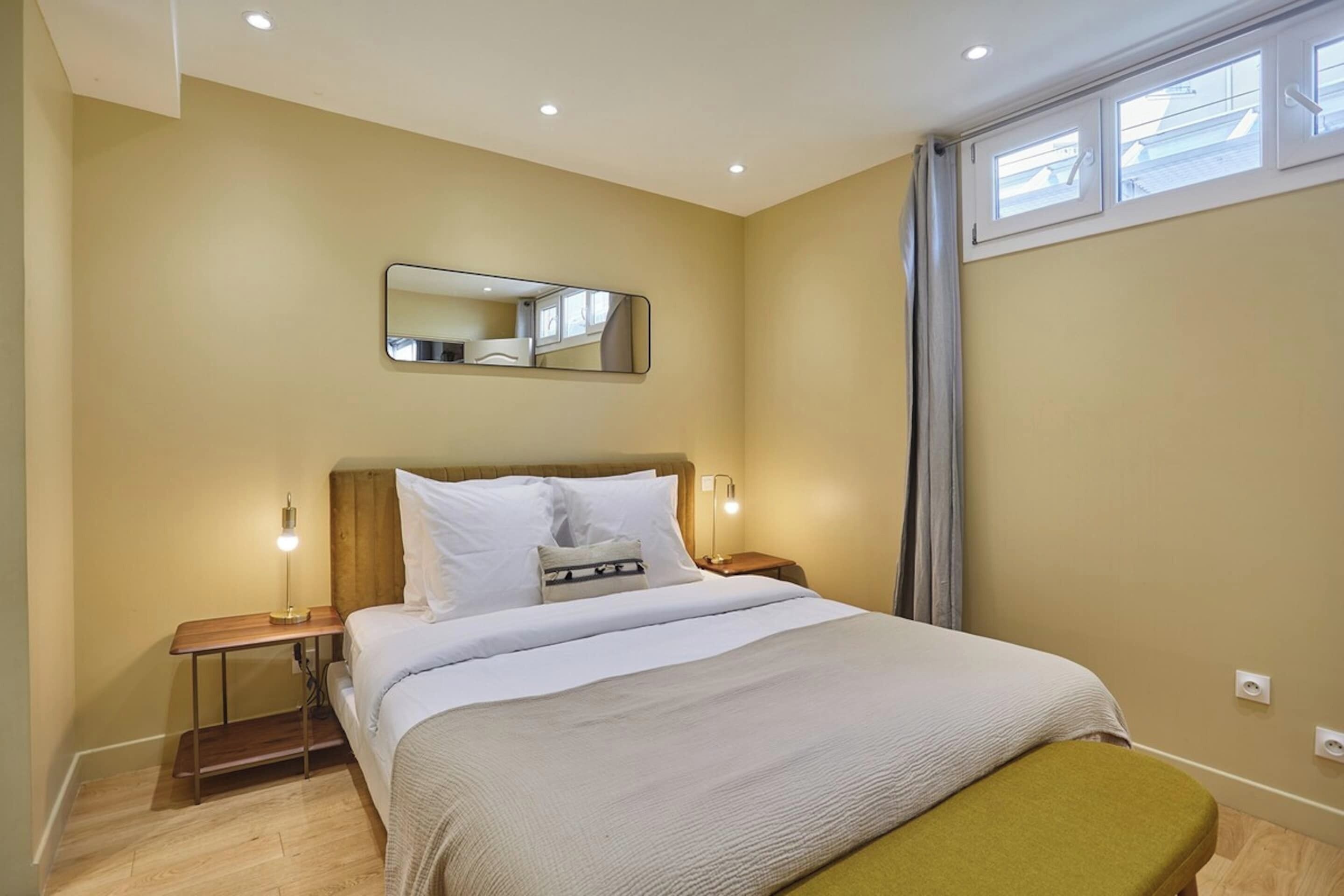 A bedroom with a bed, bedside tables, a mirror, and a window.