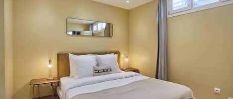 A bedroom with a bed, bedside tables, a mirror, and a window.