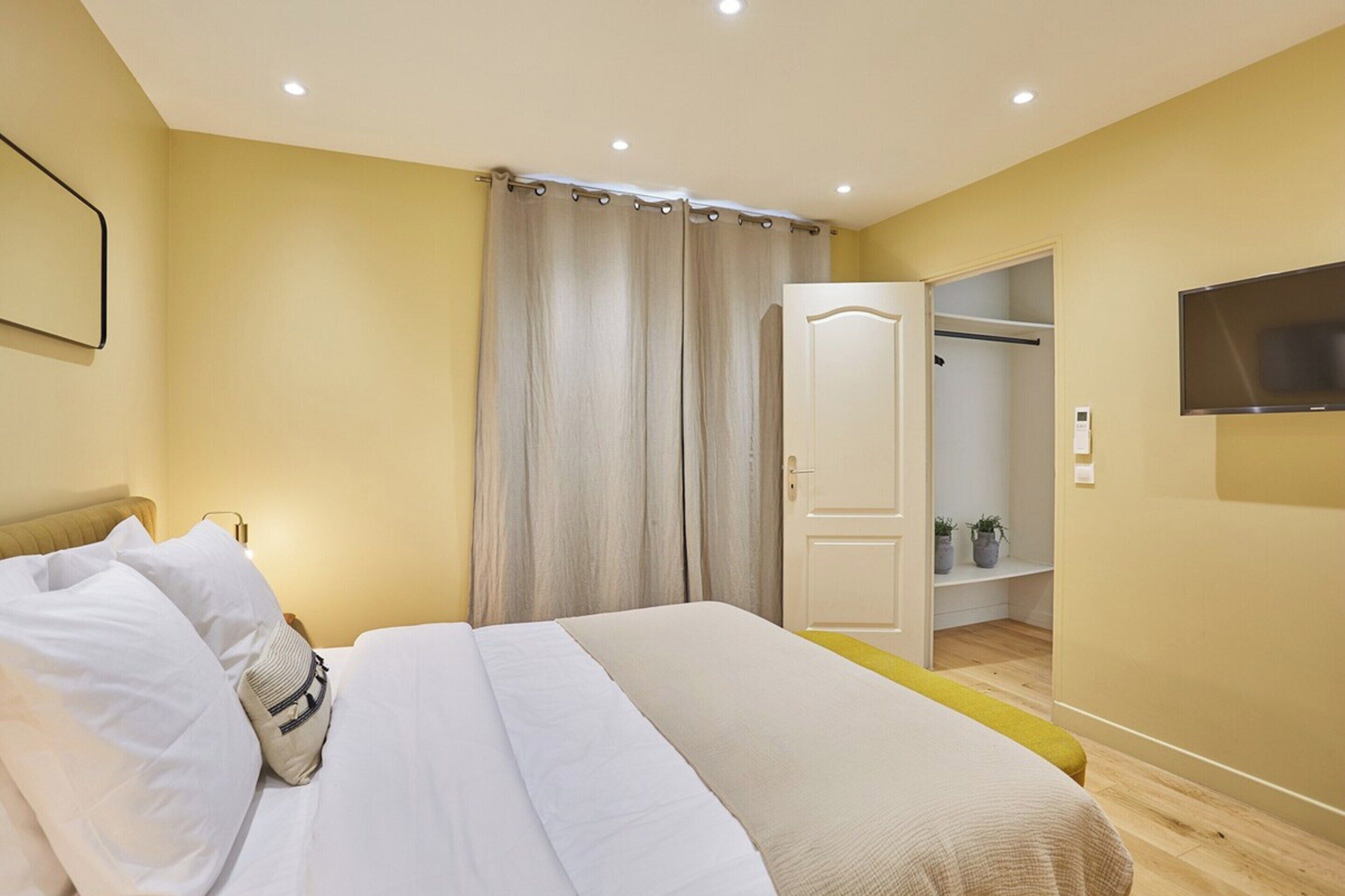 A bedroom with a bed, a wardrobe, a television, and a door leading to a closet.