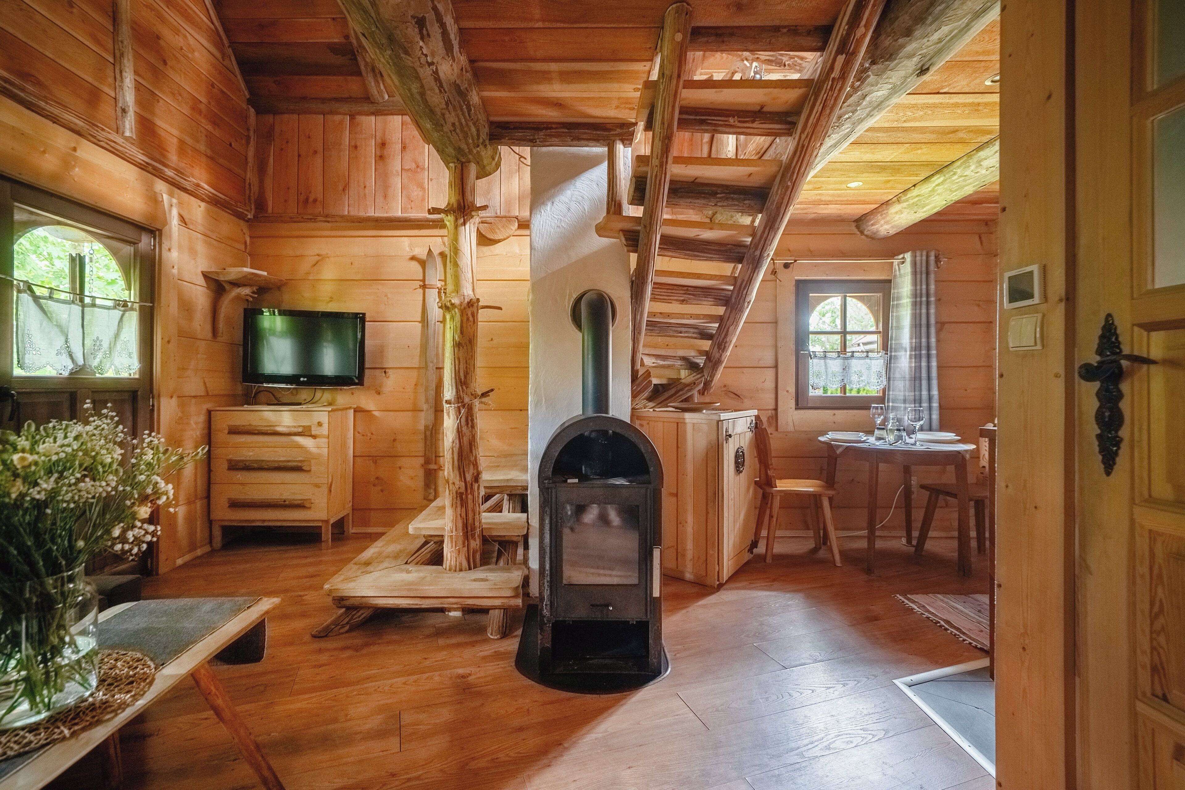 Interior de una cabaña de madera con chimenea, muebles de madera, televisor y comedor.