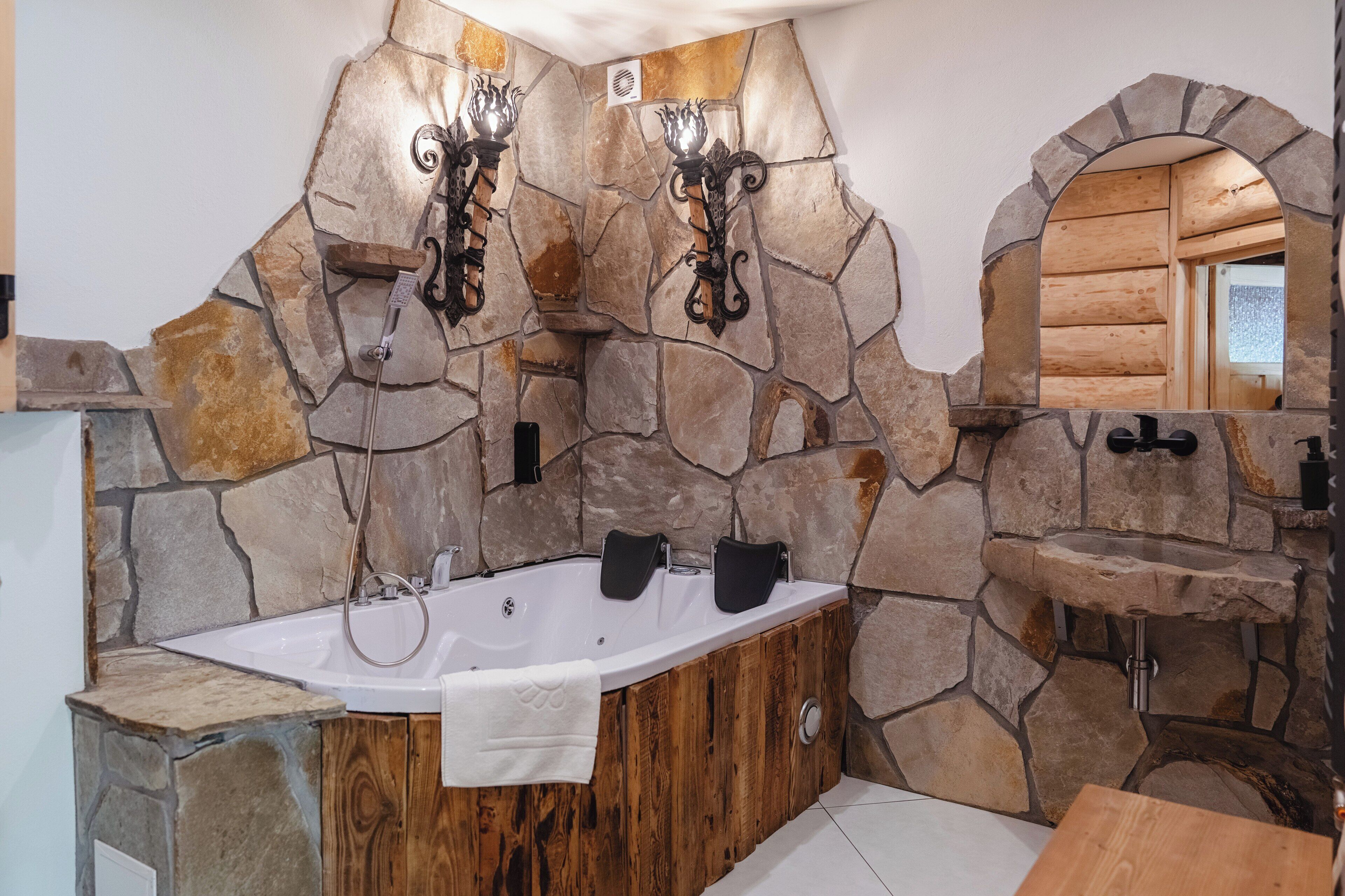 Une salle de bain avec un mur en pierre, une baignoire en bois, un lavabo et un miroir.