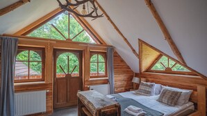 Een gezellig slaapkamer op zolder met een houten bed, een bankje en grote ramen met uitzicht op het groen.