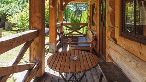 Een houten terras met een ronde tafel en bankjes, omgeven door houten wanden en een raam.