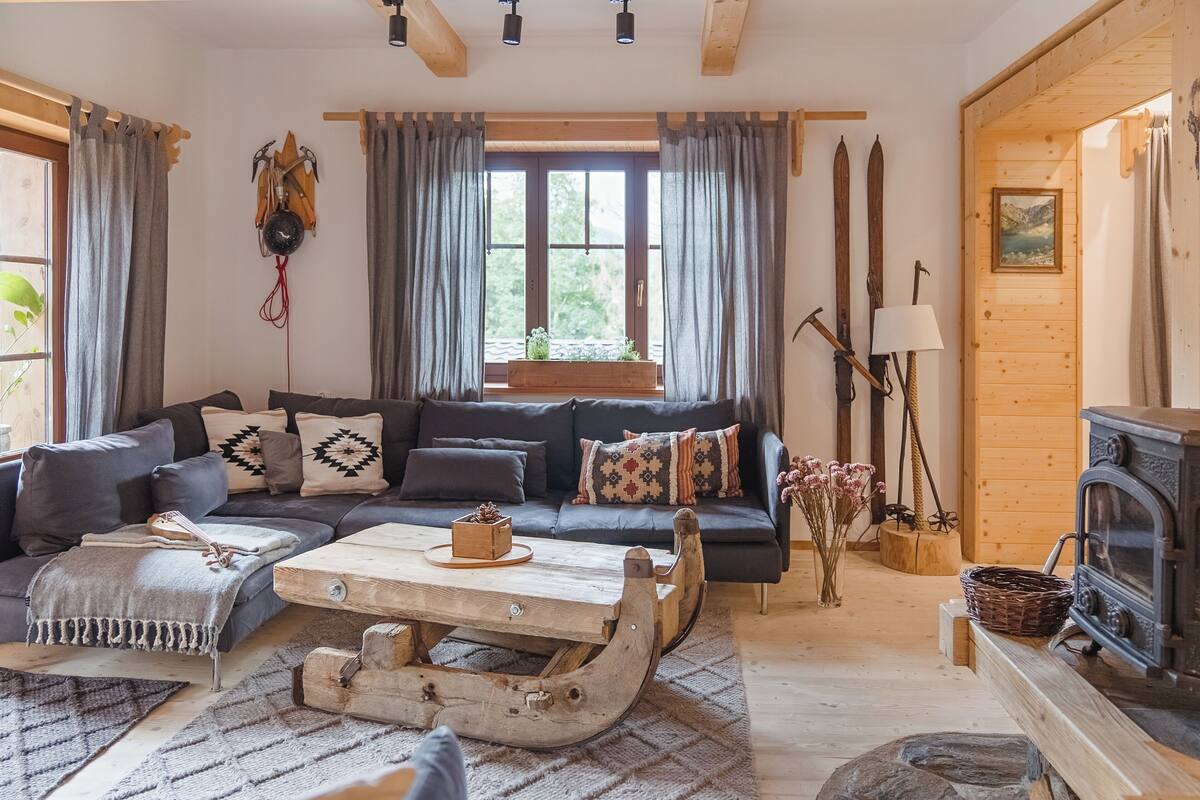 Een gezellige woonkamer met een donkergroene bank, een houten salontafel en een rustieke open haard.