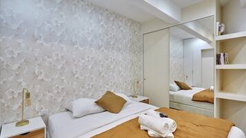 A modern hotel room with a large bed, a nightstand, a mirror, and a bookshelf.