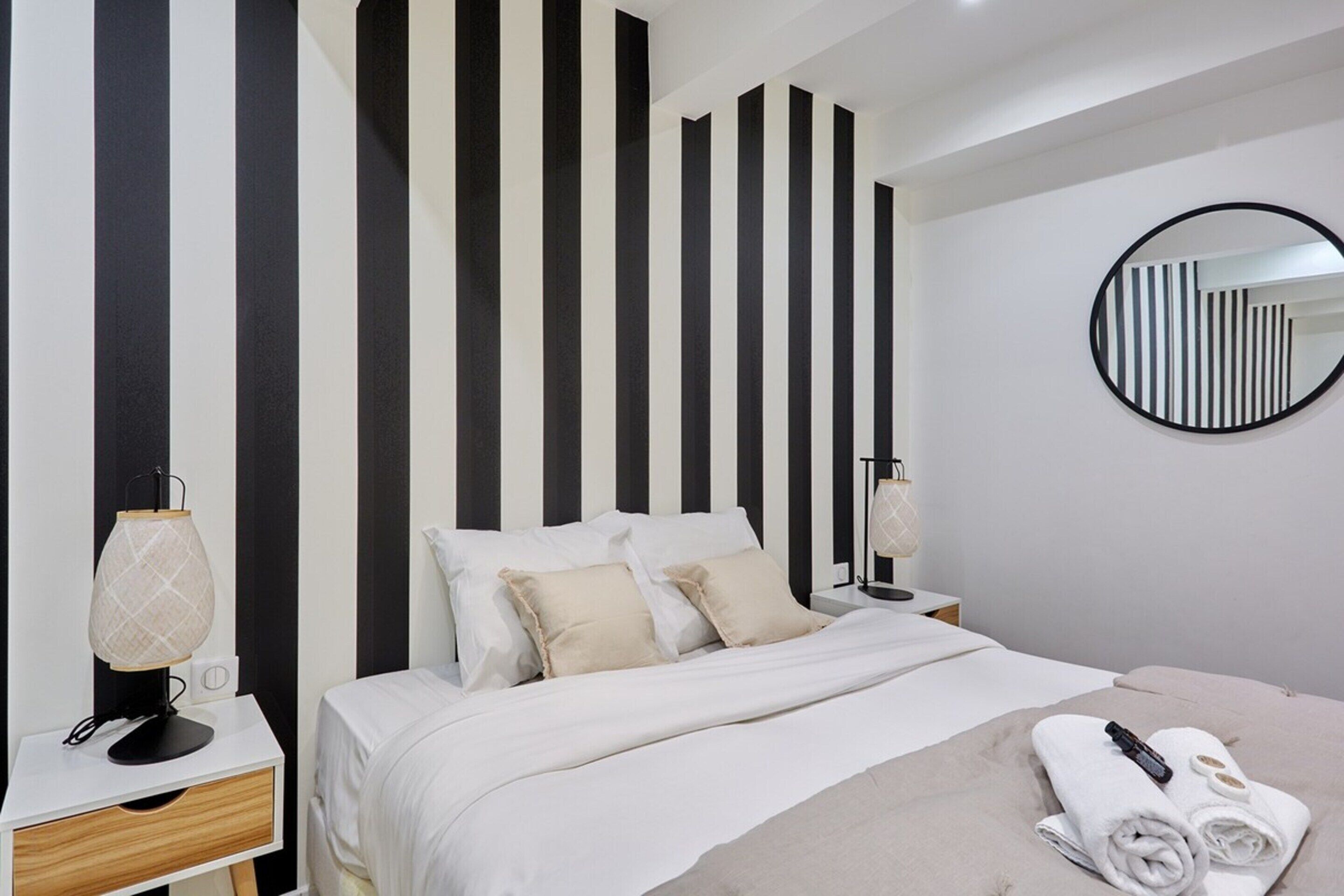 Une chambre à coucher moderne avec un lit, des tables de chevet, une lampe, un miroir et des serviettes.