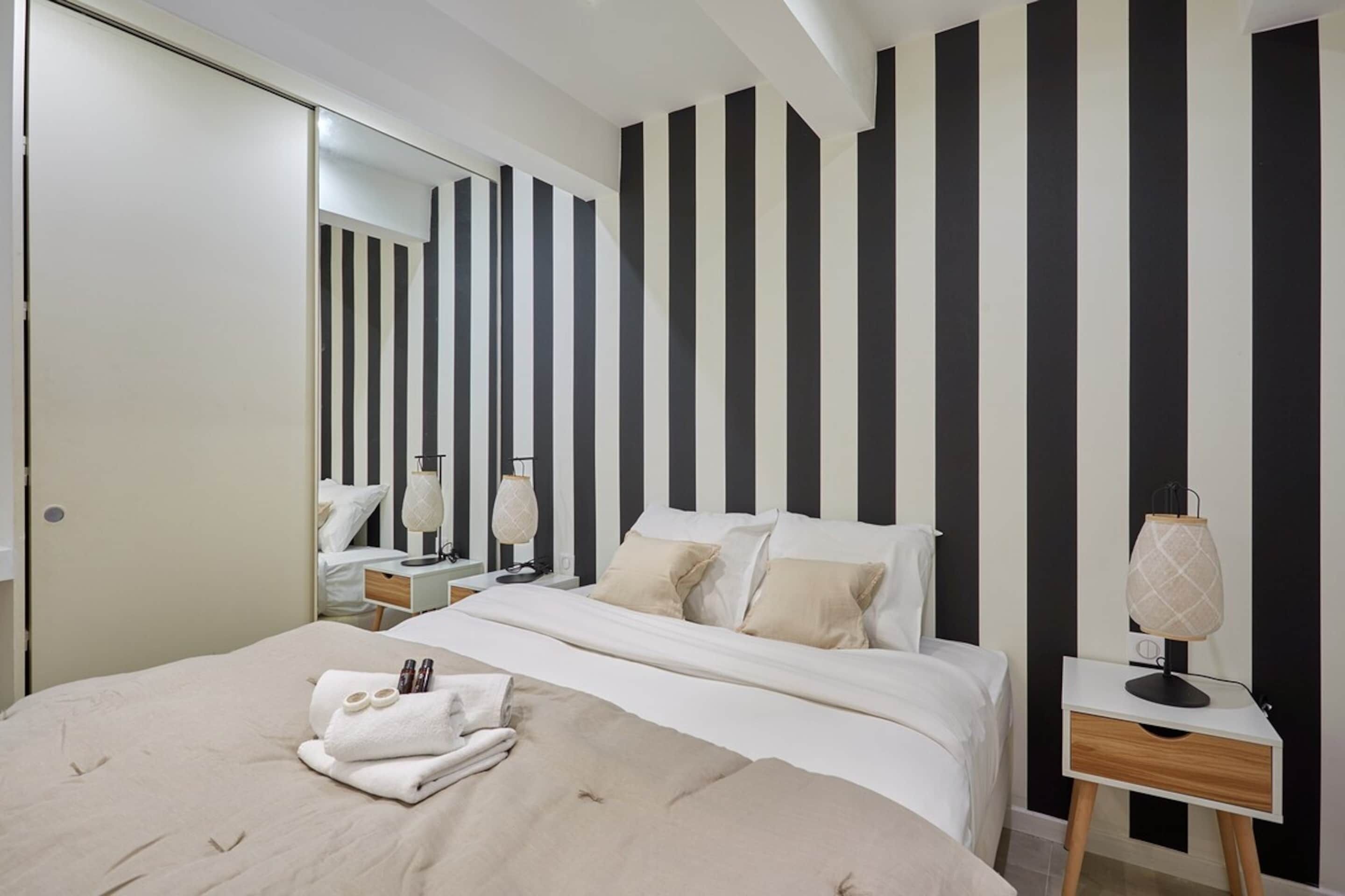 Una camera d'hotel con un letto, comodini, uno specchio e una parete a righe.