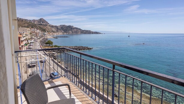 A balcony with a clear view of a coastal town, rocky shoreline, and calm sea.