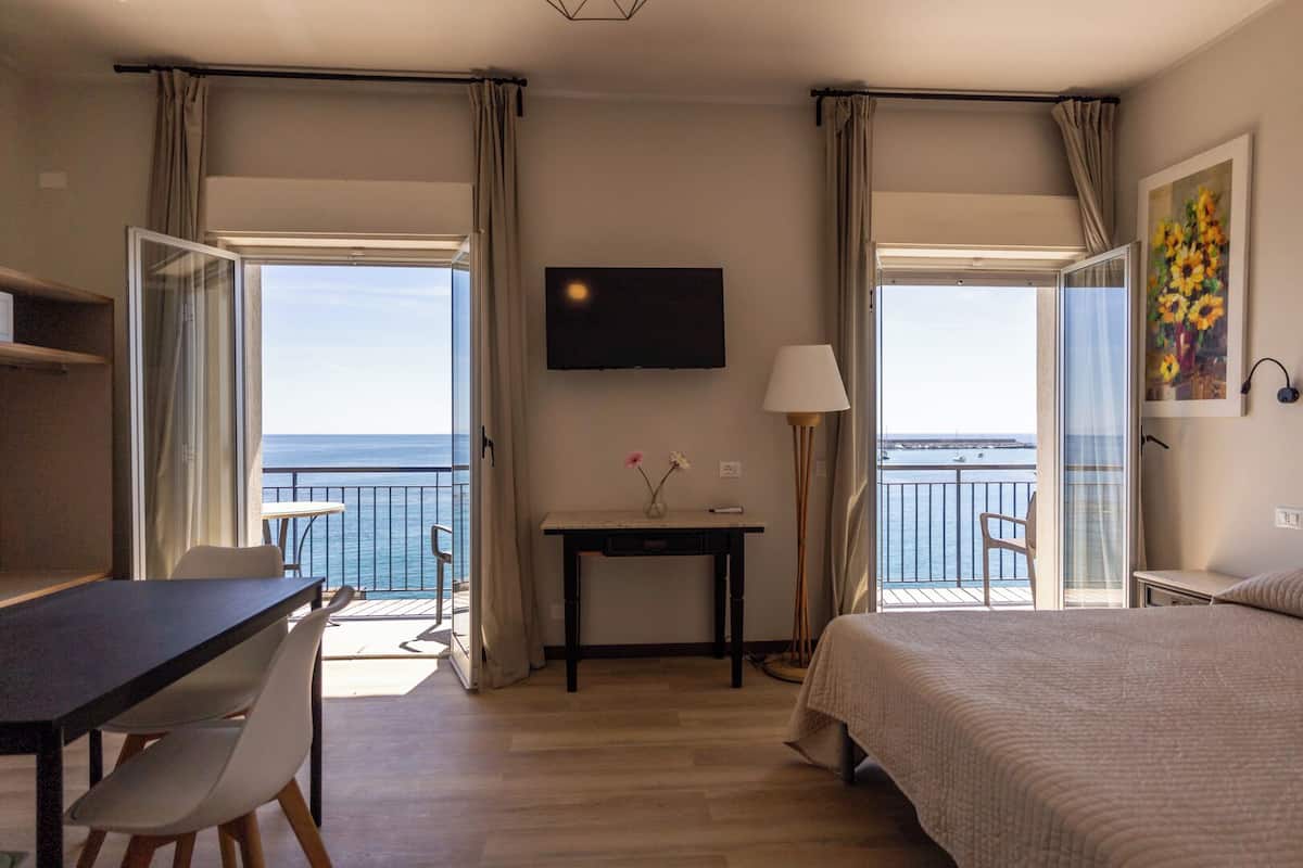 Ein Hotelzimmer mit Bett, Schreibtisch, Stuhl, Tisch mit Vase, Lampe und Fernseher an der Wand.