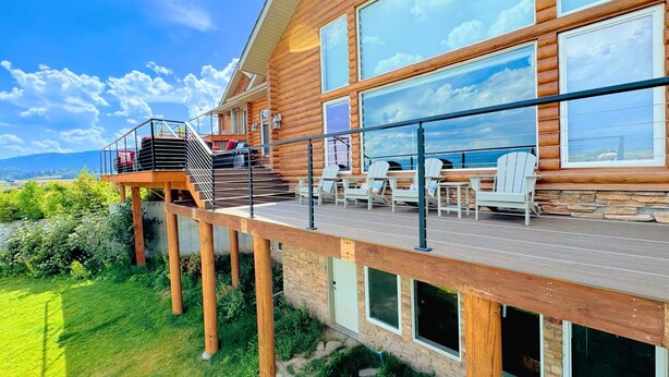 Una cabaña de madera con terraza, asientos exteriores y ventanas grandes.