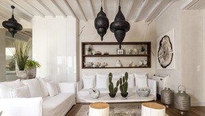 Una sala de estar moderna con un sofá blanco, dos taburetes de madera, una mesa de centro de mármol y objetos decorativos en estanterías.