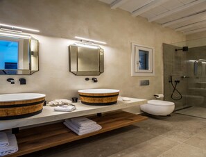 Un baño moderno con dos lavamanos redondos de madera, una ventana pequeña y una zona de ducha con mampara de cristal.