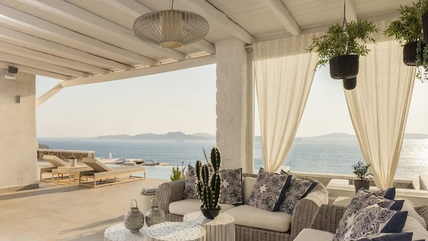 Una terraza soleada con vistas al mar, amueblada con un sofá, una mesa de centro y plantas colgantes.