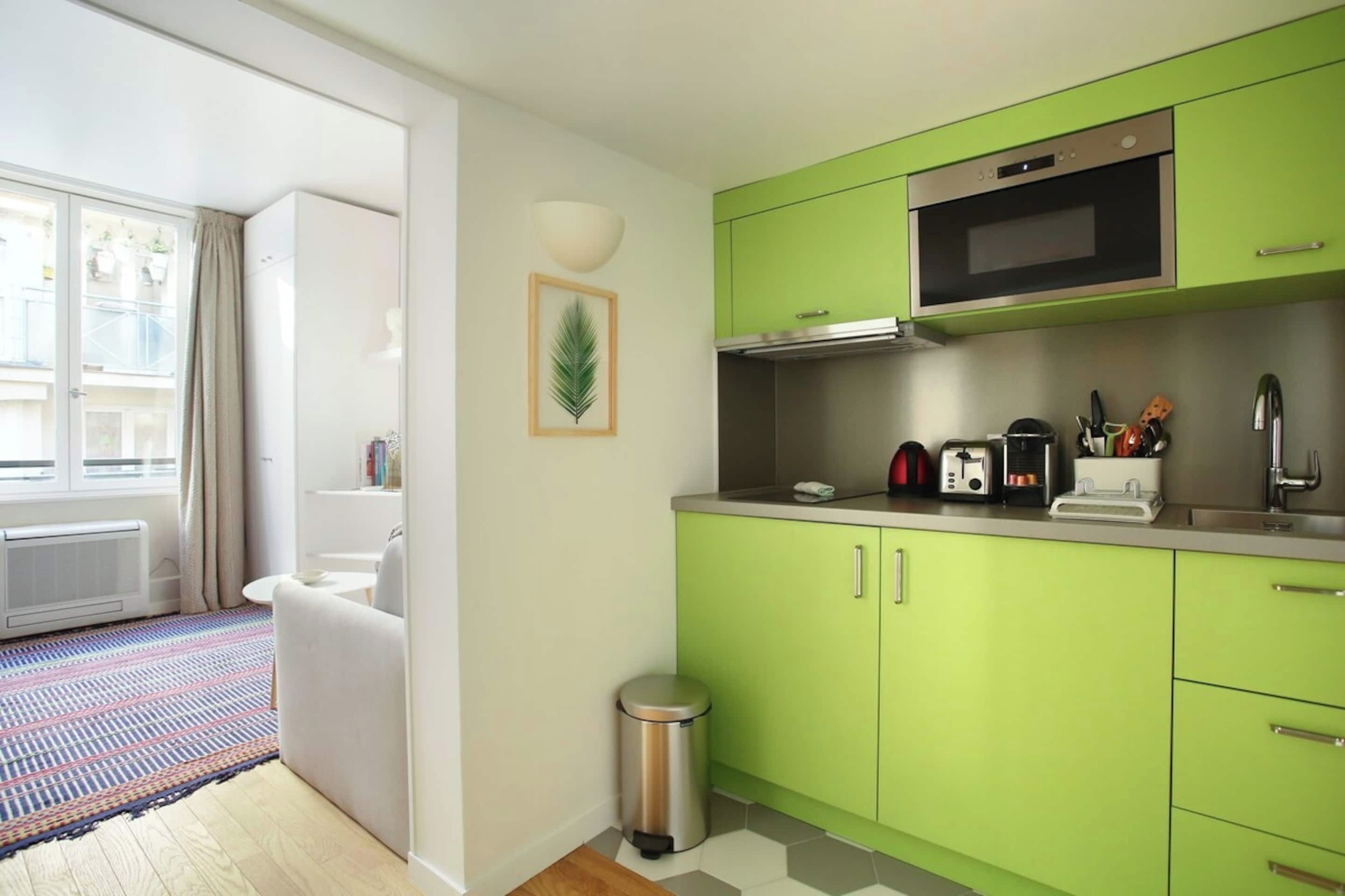 A compact kitchen with green cabinets, a stainless steel oven, and a small countertop with a kettle and toaster.