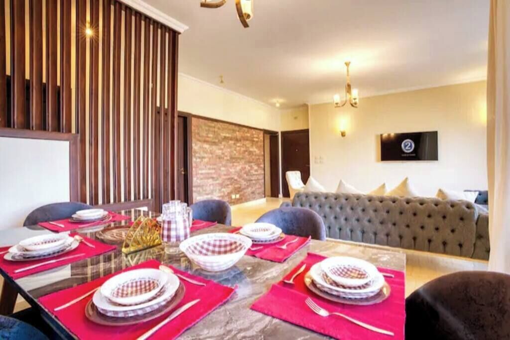 Un comedor con una mesa de vidrio preparada para cuatro, individuales rojos y un sofá gris al fondo.