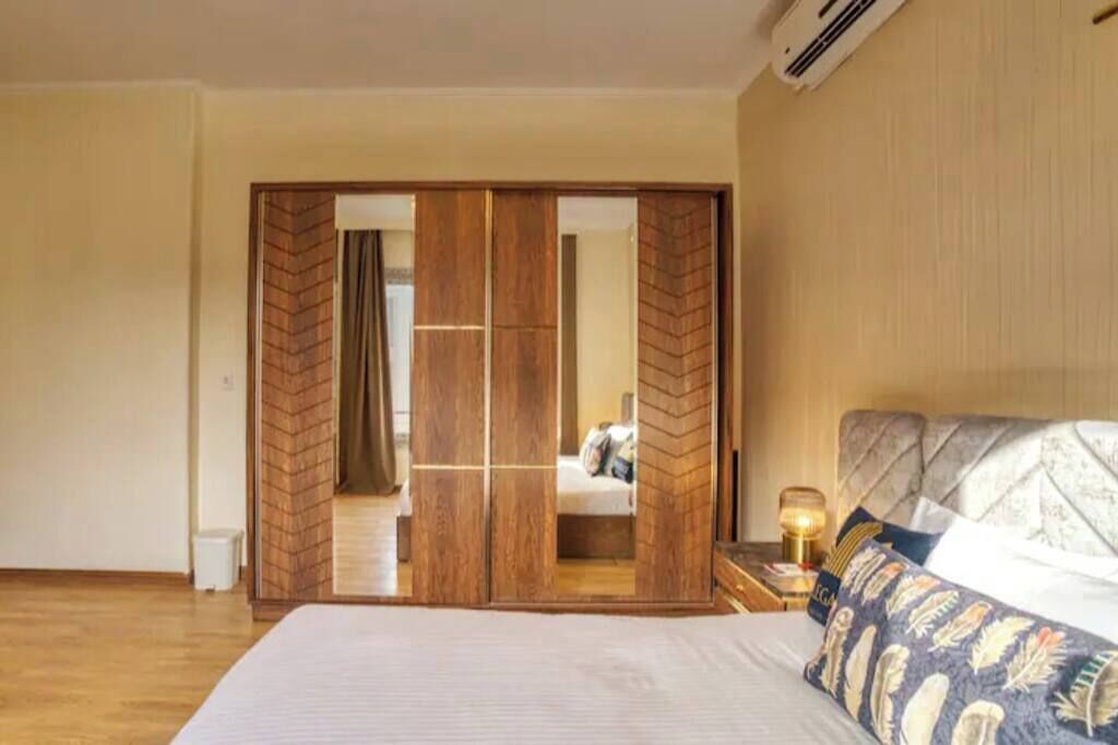 A bedroom with a bed, a nightstand with a lamp, and a wooden wardrobe with a mirror.