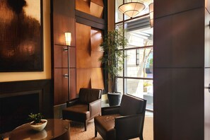 A lobby with a modern design, featuring a large wooden panel wall, a floor lamp, a potted plant, and seating arrangements.