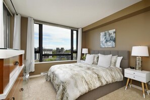 Ein modernes Hotelzimmer mit einem großen Bett, zwei Nachttischlampen und Blick auf eine Stadtlandschaft sowie eine Stadtbrücke durch das Fenster.